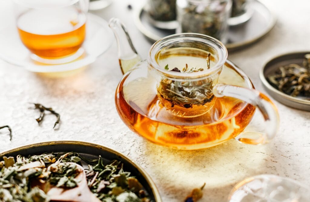 Butelka z herbatą na stole, herbaty liściowe i zaparzacz, zdjęcie w jasnej tonacji.