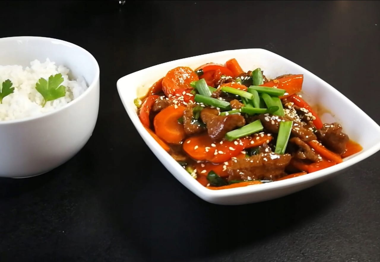 UB Sos Chilli Sechuan Fusion 400g 5 Pyszne danie azjatyckie z warzywami i mięsem w orientalnym sosie, podawane z białym ryżem na czarnym tle.