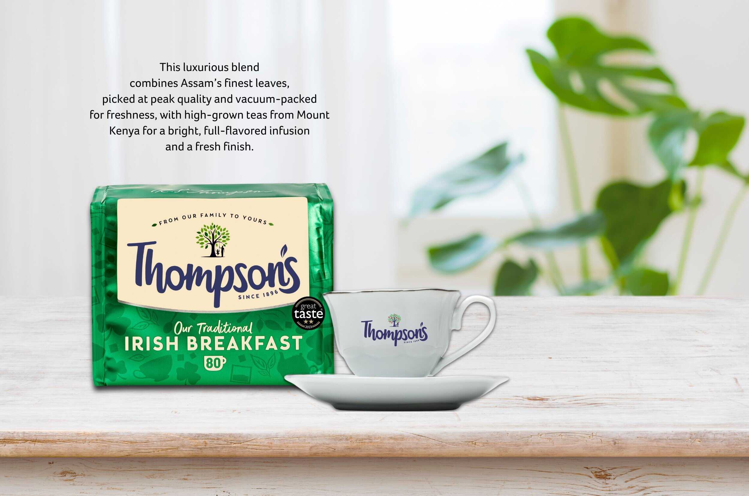 Paczka herbaty Thompsons Irish Breakfast na białym tle z filiżanką herbaty na stole, opis jakości i naturalnych składników herbaty z Assam i Mount Kenya.